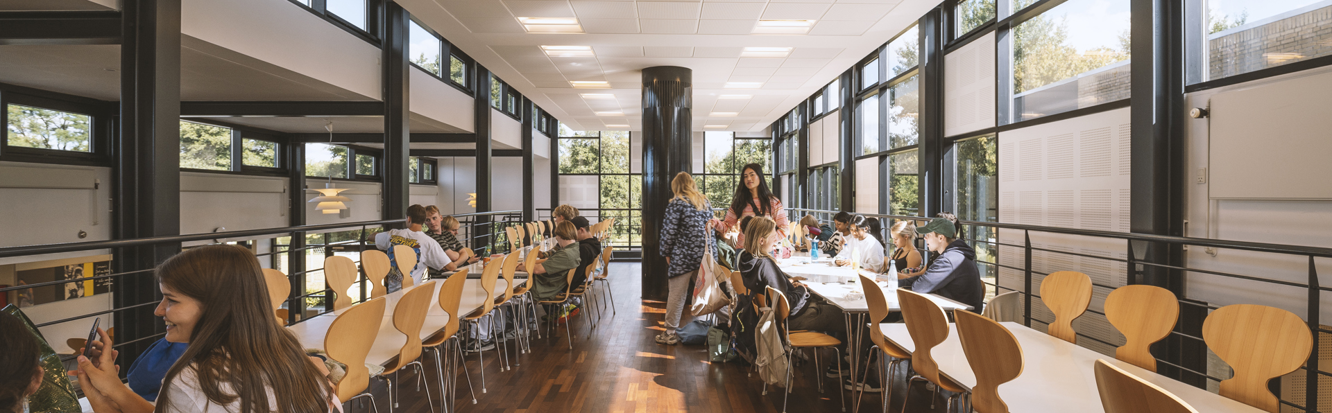 Unge mennesker sidder ved borde i lyst fællesområde og arbejder eller snakker