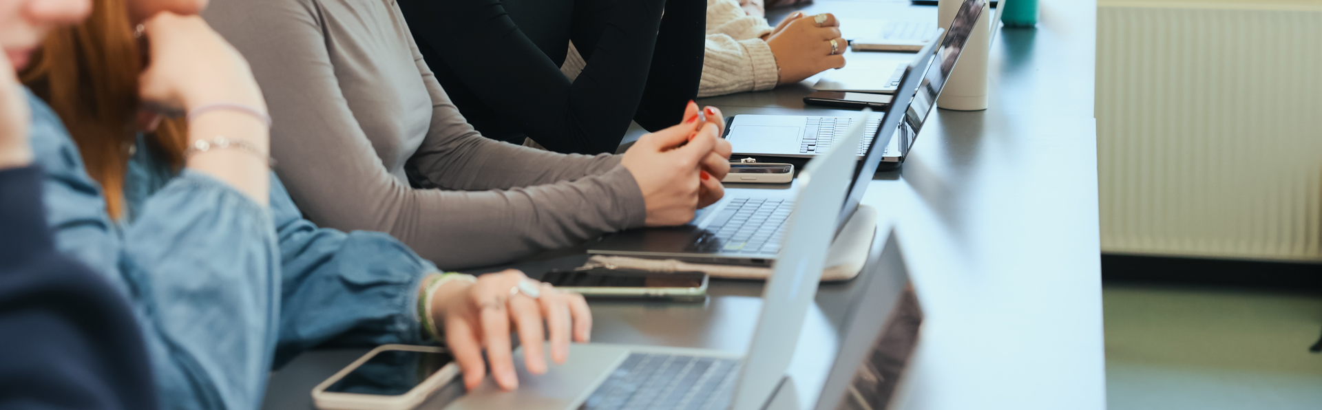 Unge studerende sidder ved computer  i undervisningslokale og lytter koncentreret til undervisningen.