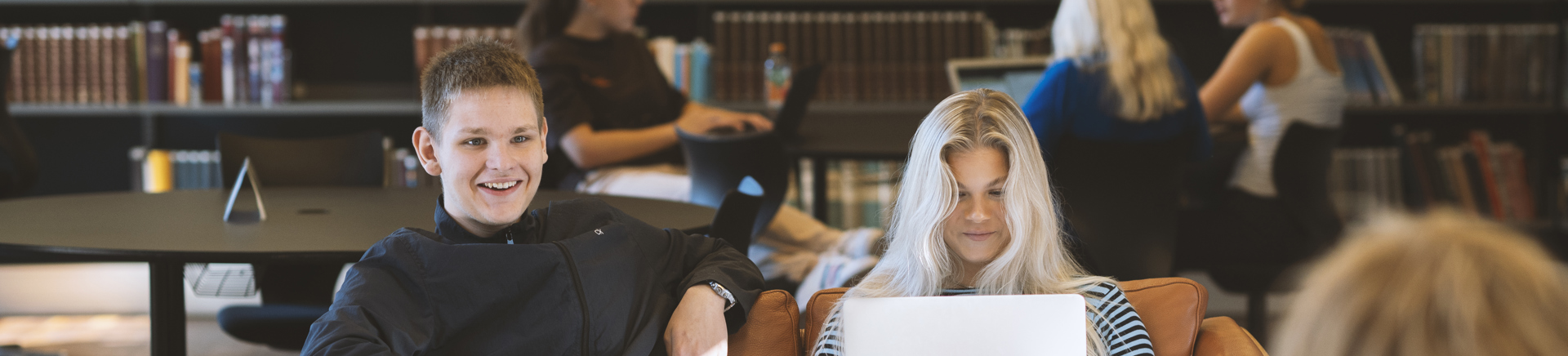 Studerende sidder i sofa og bruger bærbare computere i biblioteksmiljø